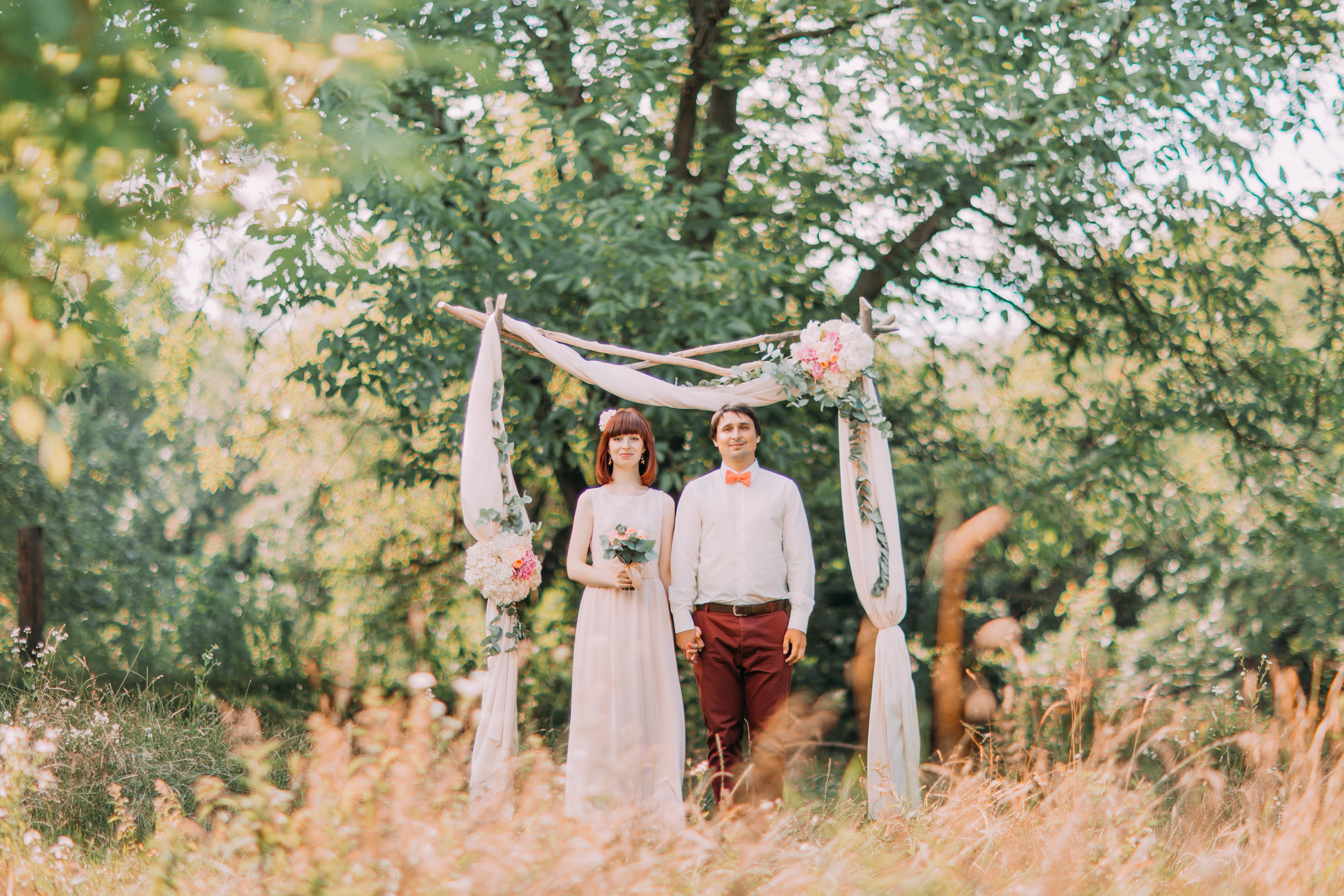 Stylish happy newlyweds holding hands on the wedding ceremony outdoors